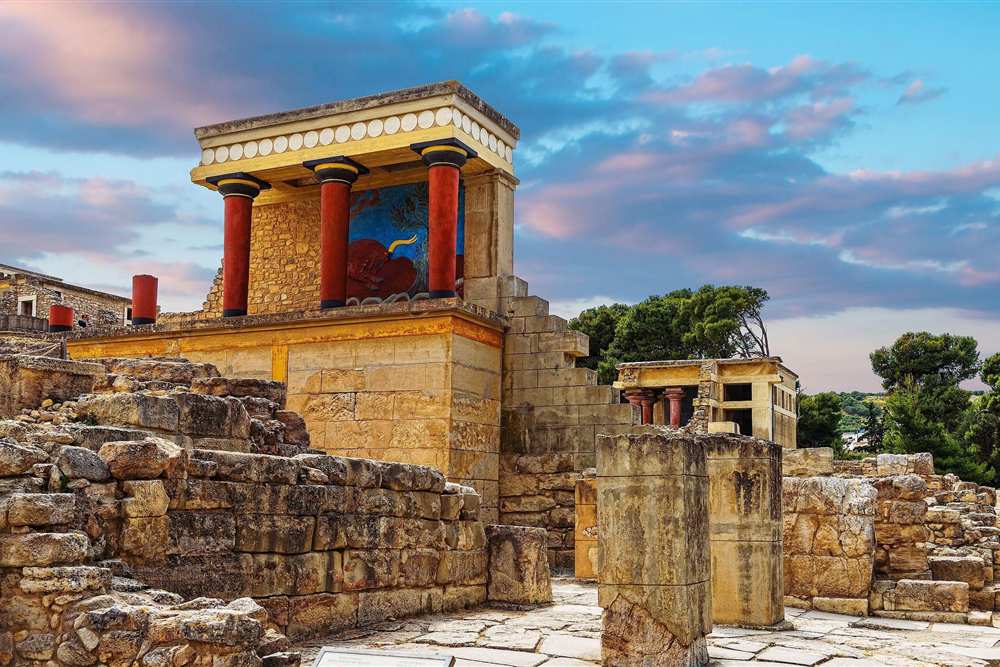 Mykonos, Santorini, Crete and Rhodes tour: the restored north entrance of the Palace of Knossos on Crete, red columns and a bull fresco above the stone ruins