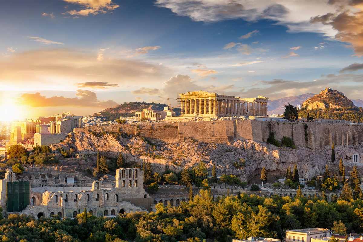 Greece and Turkey tour: the Parthenon and the other temples on the Acropolis hill of Athens at sunset, with an ancient theatre below and green trees in the foreground