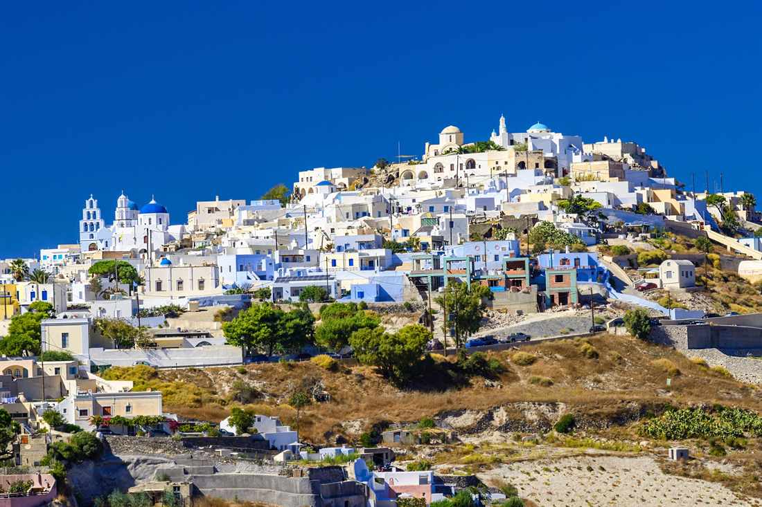 4 day Santorini Greek tour: the whitewashed hill village of Pyrgos, with blue-domed churches and bell towers on the summit, under a deep blue sky on Santorini island