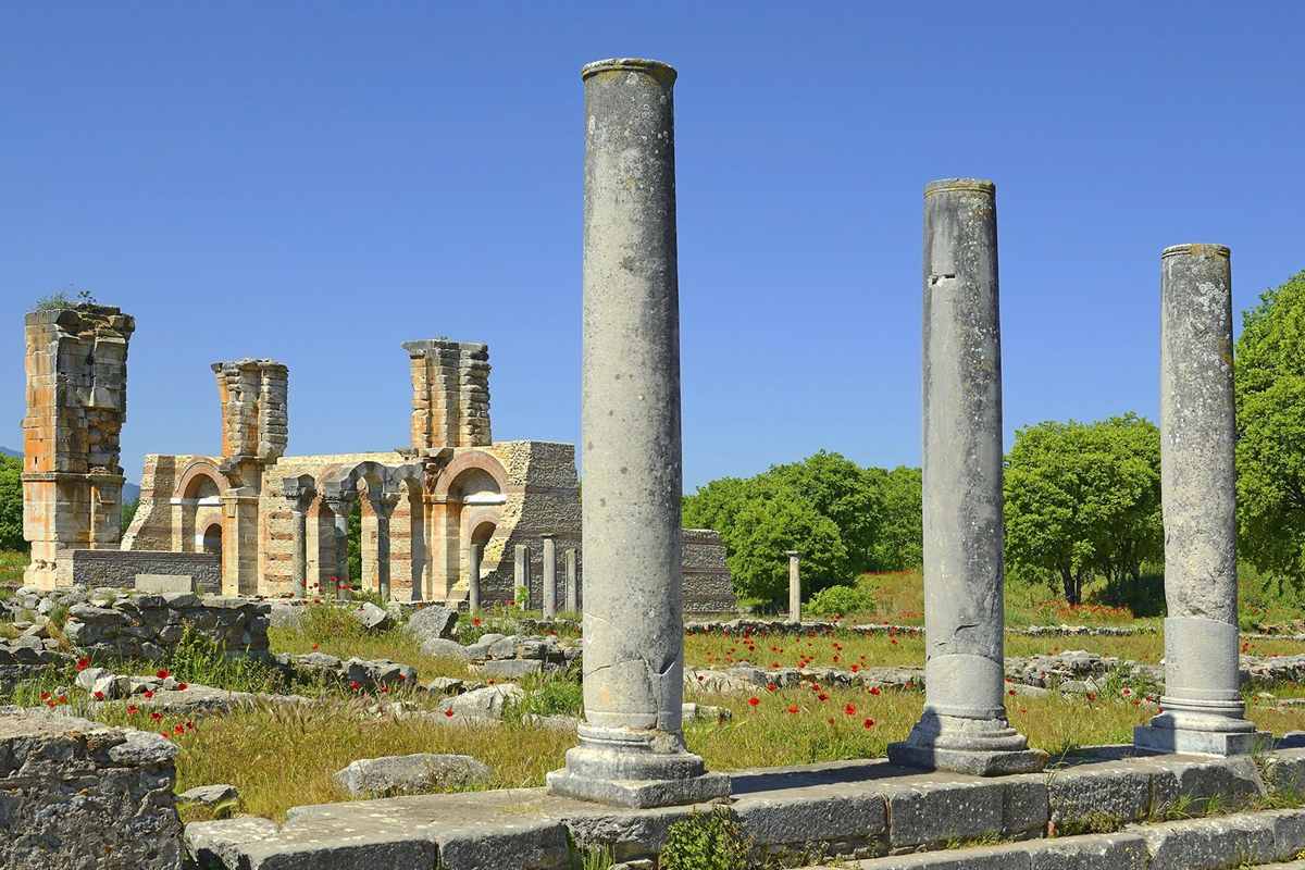 Kavala and Philippi day trip: three tall grey stone columns in the foreground at Philippi, with the tall piers and arches of ruined brick and pale stone behind them, red poppies in the grass and a clear blue sky