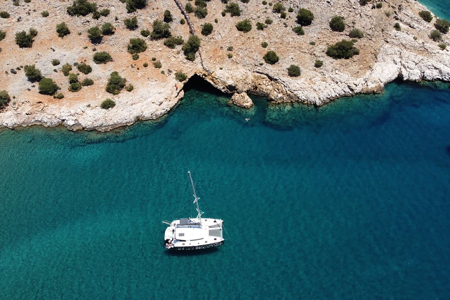 Naxos catamaran cruise: a white catamaran anchored in a turquoise bay below a rocky white cliff with a sea cave