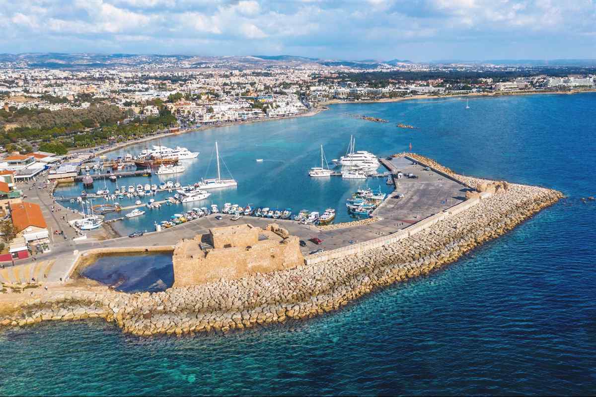 Paphos glass bottom boat: an aerial view of Paphos harbour in Cyprus, with the square sandstone castle on a long rock breakwater, yachts and small fishing boats moored in the bay, the white town behind and deep blue sea in front