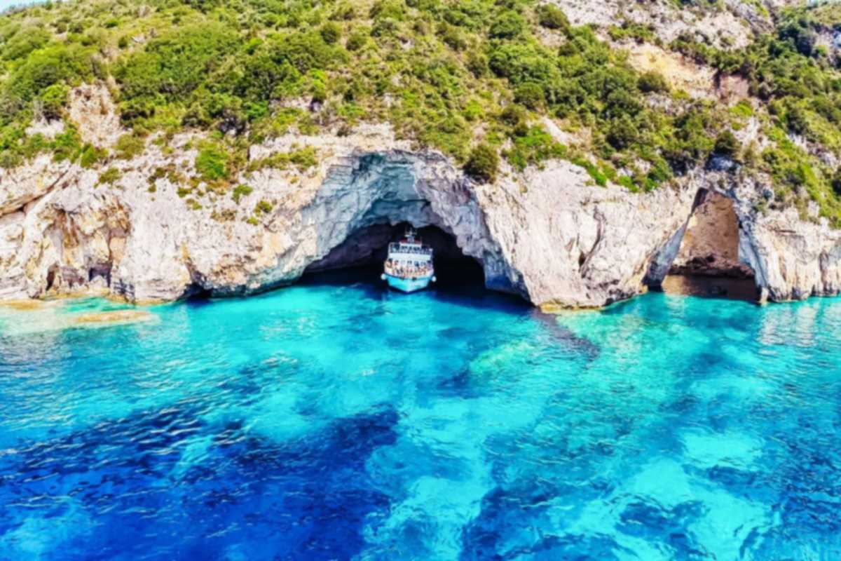 Paxos Antipaxos Blue Caves cruise from Corfu: a white tour boat inside a wide sea-cave arch in white limestone cliffs above turquoise water