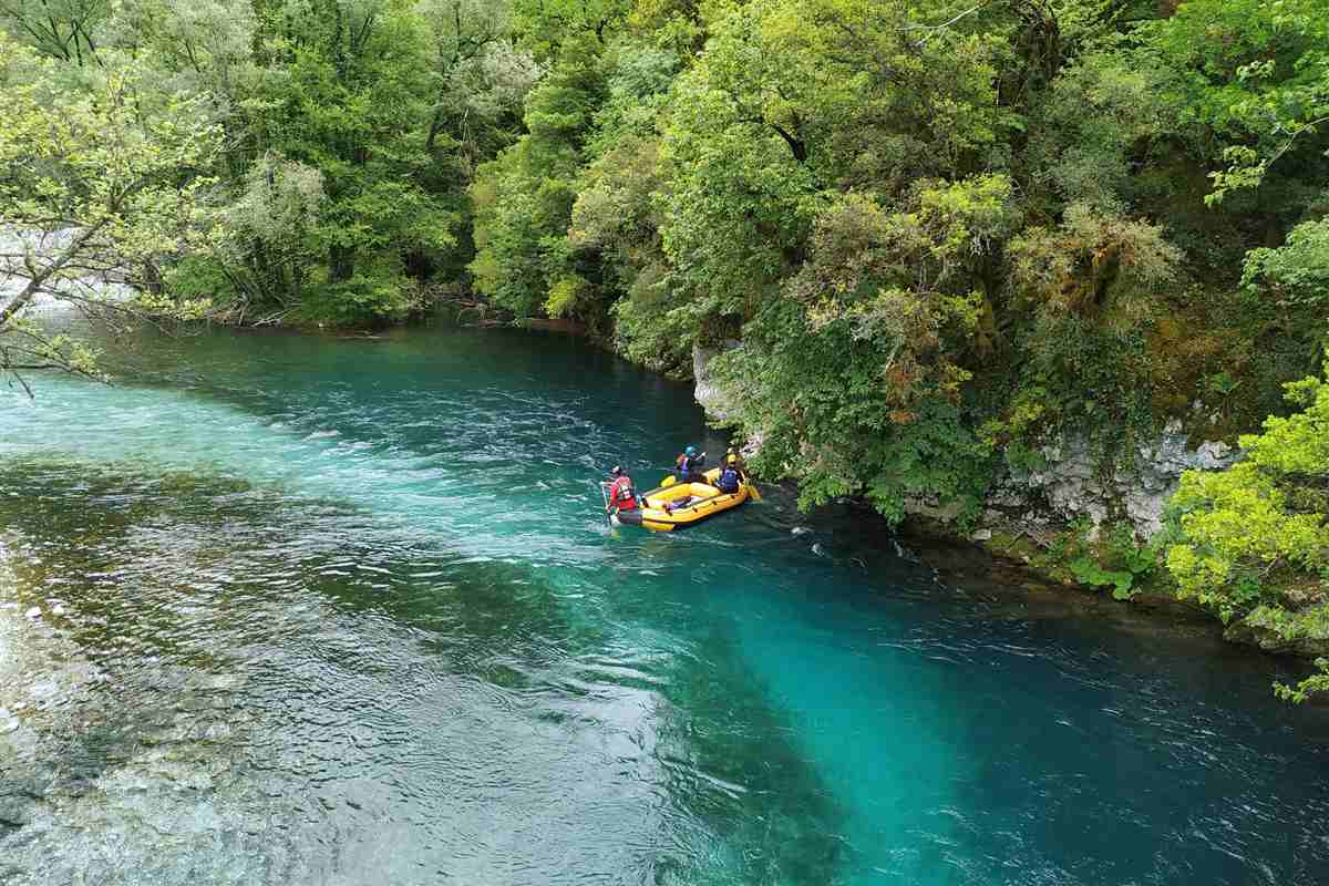 Voidomatis rafting: a yellow raft with a small crew in helmets and life jackets paddling on bright turquoise river water beside a pale rock bank and dense green trees